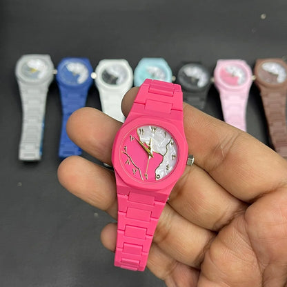 Close-up of a pink women's wrist watch featuring a marble pattern dial, gold hands, and a matching silicone strap, with multiple color variants displayed in the background.