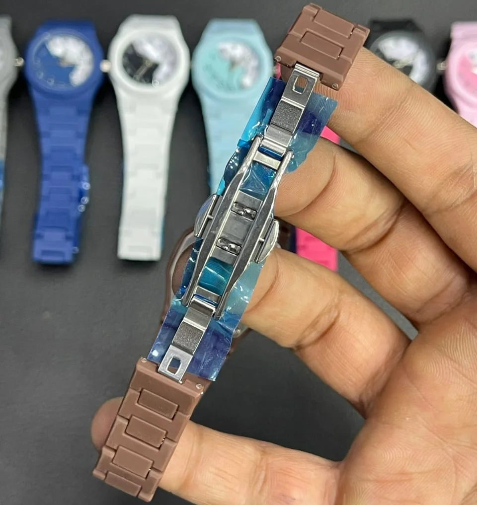 Close-up view of a stylish wristwatch showing its secure stainless steel folding clasp and durable strap design. The watch is held in hand with multiple color variants displayed in the background, highlighting comfort, durability, and everyday fashion appeal.