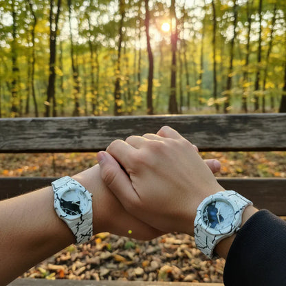Couple wearing matching white marble pattern wrist watches while holding hands on a park bench at sunset, showcasing a stylish his and hers watch set with elegant round dials.